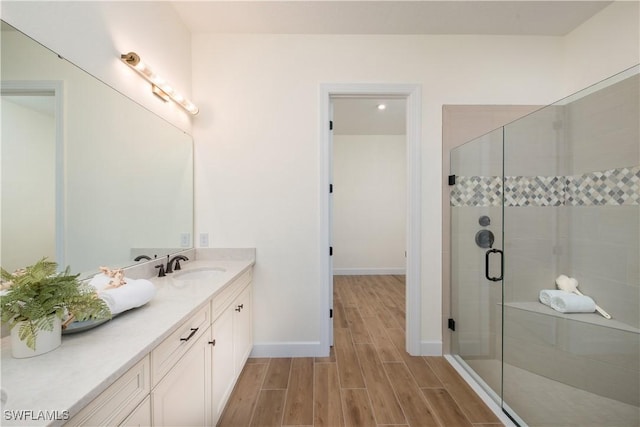 bathroom with wood finish floors, a shower stall, vanity, and baseboards