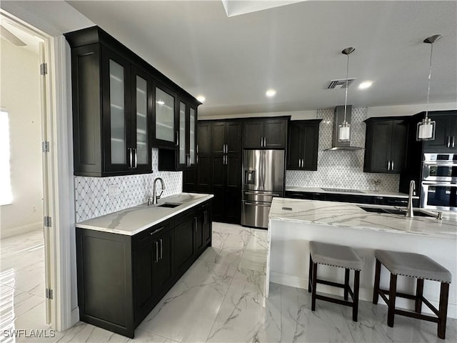 kitchen featuring wall chimney exhaust hood, a breakfast bar, sink, hanging light fixtures, and appliances with stainless steel finishes