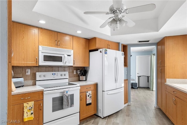 kitchen with white appliances, light hardwood / wood-style flooring, ceiling fan, a tray ceiling, and decorative backsplash