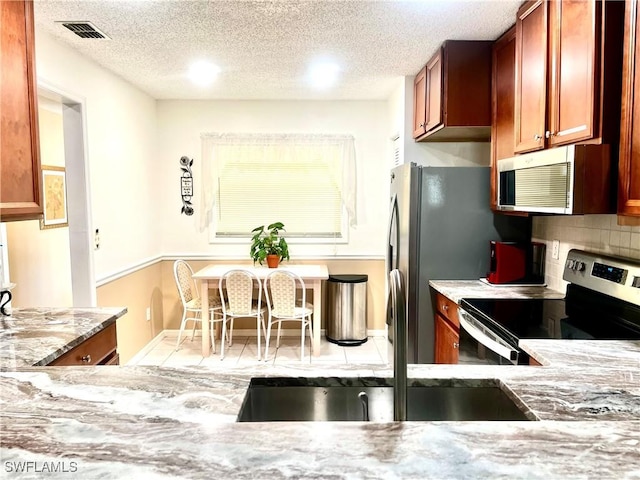 kitchen featuring sink, appliances with stainless steel finishes, light stone counters, a textured ceiling, and decorative backsplash