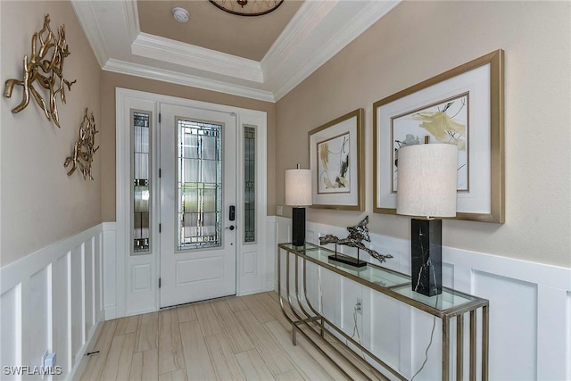 entryway featuring a decorative wall, ornamental molding, light wood-type flooring, wainscoting, and a tray ceiling