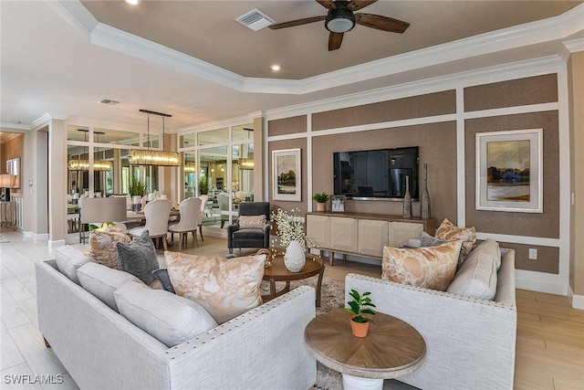 living area featuring visible vents, ornamental molding, a tray ceiling, light wood-type flooring, and ceiling fan with notable chandelier