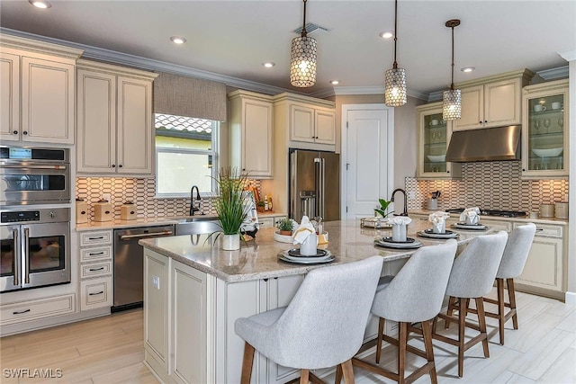 kitchen featuring glass insert cabinets, under cabinet range hood, a center island with sink, and appliances with stainless steel finishes