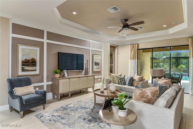 living area with ornamental molding, a raised ceiling, visible vents, and a ceiling fan