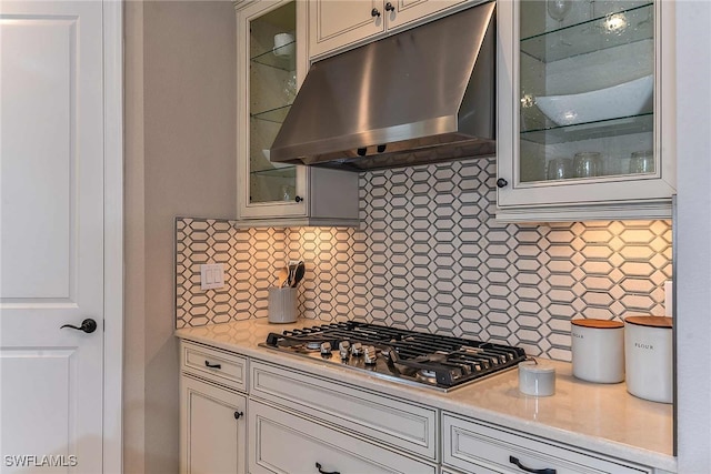 kitchen with glass insert cabinets, light countertops, stainless steel gas cooktop, and under cabinet range hood