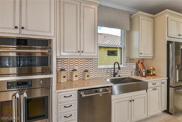 kitchen featuring stainless steel appliances, light countertops, backsplash, cream cabinets, and a sink