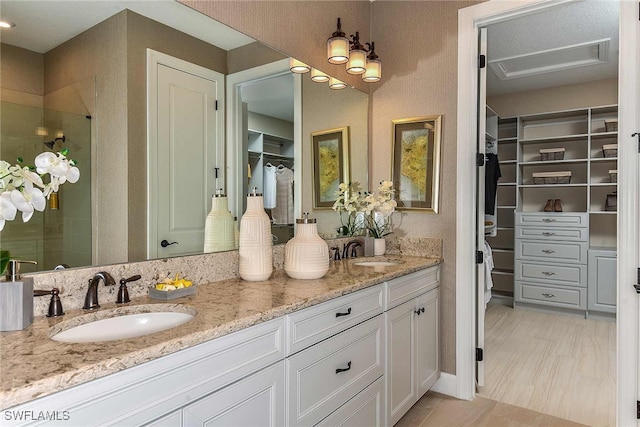 bathroom featuring a sink, a spacious closet, a shower stall, and double vanity