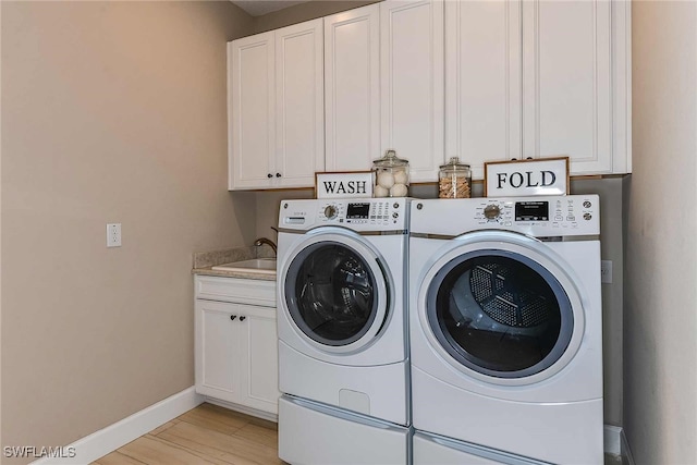 clothes washing area with washing machine and dryer, a sink, baseboards, cabinet space, and light wood finished floors