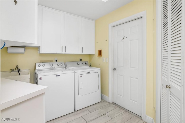 washroom featuring washer and clothes dryer, cabinet space, wood tiled floor, a sink, and baseboards