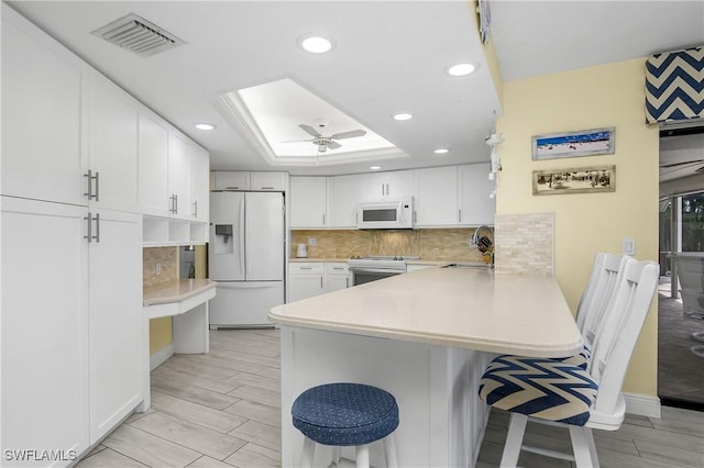 kitchen with white appliances, a skylight, visible vents, a peninsula, and a sink