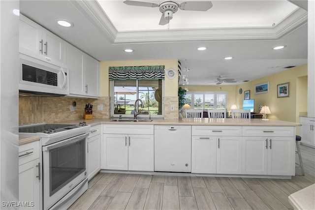 kitchen with a tray ceiling, light countertops, white cabinets, white appliances, and a peninsula