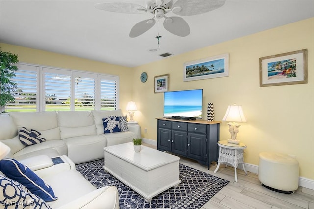 living area with visible vents, light wood-style flooring, a ceiling fan, and baseboards