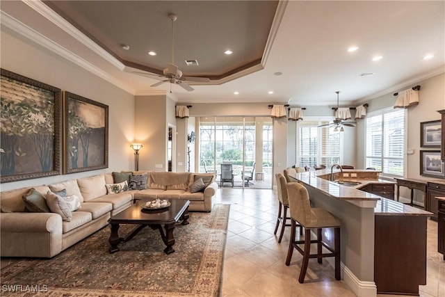 living room featuring a raised ceiling, ornamental molding, sink, and a wealth of natural light