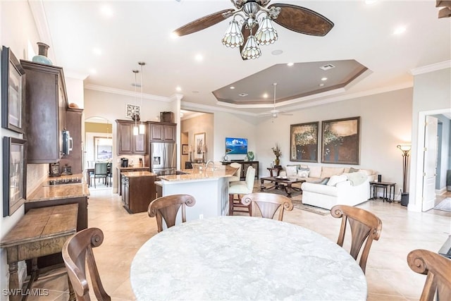 tiled dining space with ceiling fan, ornamental molding, and a tray ceiling