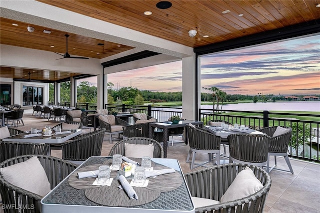 patio terrace at dusk featuring a water view, ceiling fan, and outdoor lounge area