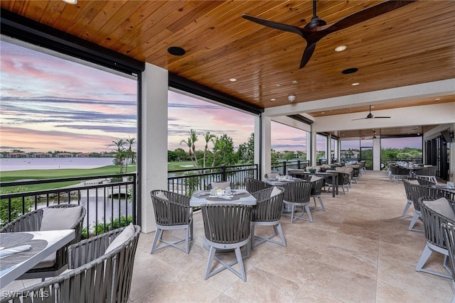 patio terrace at dusk featuring ceiling fan and a water view