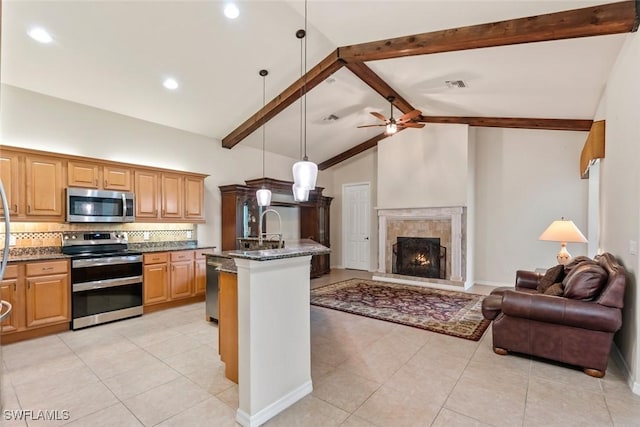 kitchen featuring appliances with stainless steel finishes, pendant lighting, tasteful backsplash, dark stone counters, and a center island with sink