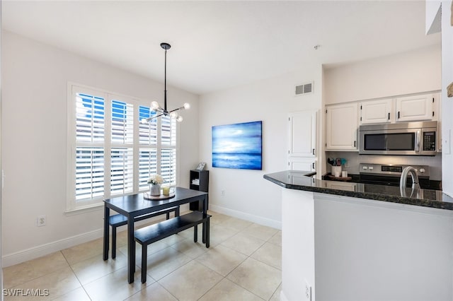 kitchen featuring appliances with stainless steel finishes, a notable chandelier, white cabinets, light tile patterned flooring, and pendant lighting