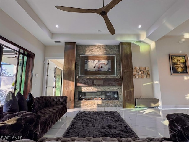 living room with a tray ceiling, a fireplace, ceiling fan, and plenty of natural light