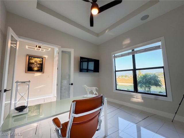 interior space with a raised ceiling, light tile patterned floors, and ceiling fan