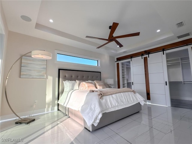 bedroom with a barn door, ceiling fan, and a tray ceiling