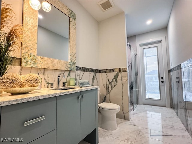 bathroom with vanity, toilet, a shower with door, and tile walls