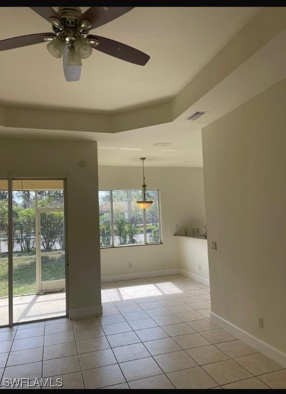 empty room featuring ceiling fan, plenty of natural light, a raised ceiling, and light tile patterned floors