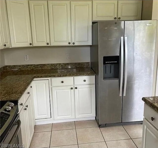 kitchen featuring light tile patterned flooring, appliances with stainless steel finishes, dark stone countertops, and white cabinets