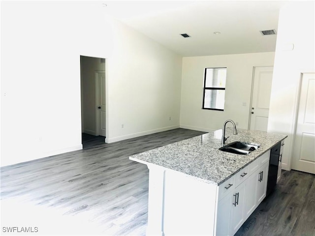 kitchen with dark wood-type flooring, sink, light stone counters, a kitchen island with sink, and white cabinets