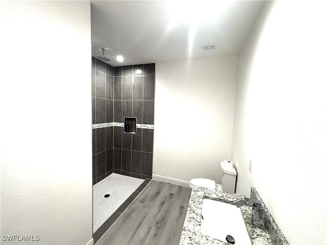 bathroom with hardwood / wood-style flooring, tiled shower, toilet, and sink