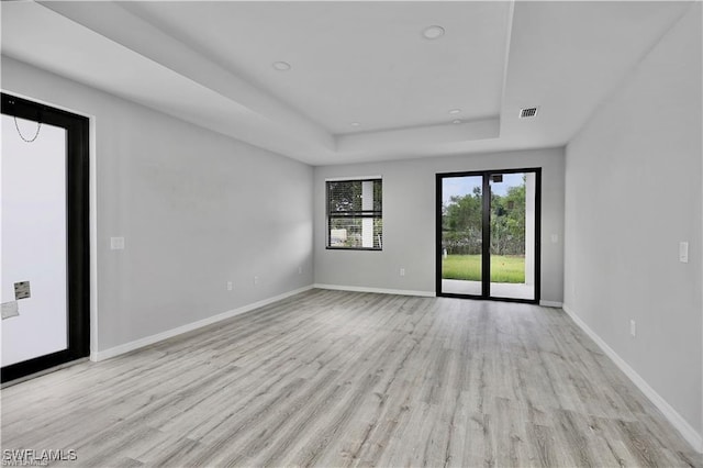 empty room with a tray ceiling and light hardwood / wood-style floors