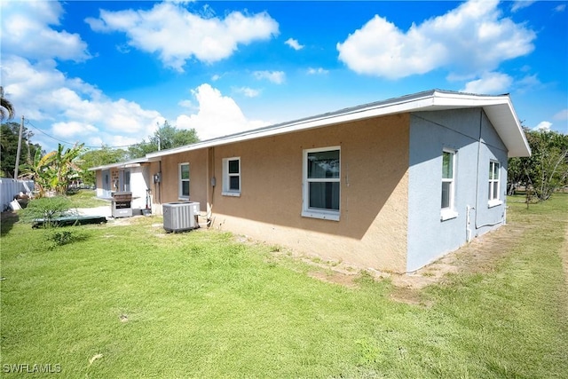 rear view of house with cooling unit, a lawn, and stucco siding