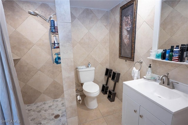 bathroom with a tile shower, vanity, toilet, tile walls, and tile patterned floors