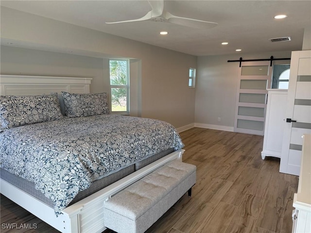 bedroom with hardwood / wood-style flooring, a barn door, and ceiling fan