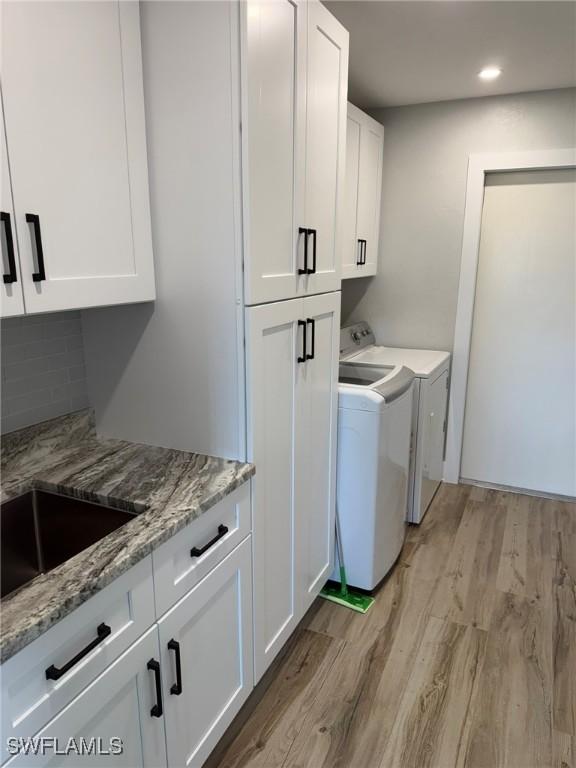 laundry room with cabinets, sink, washing machine and dryer, and light wood-type flooring