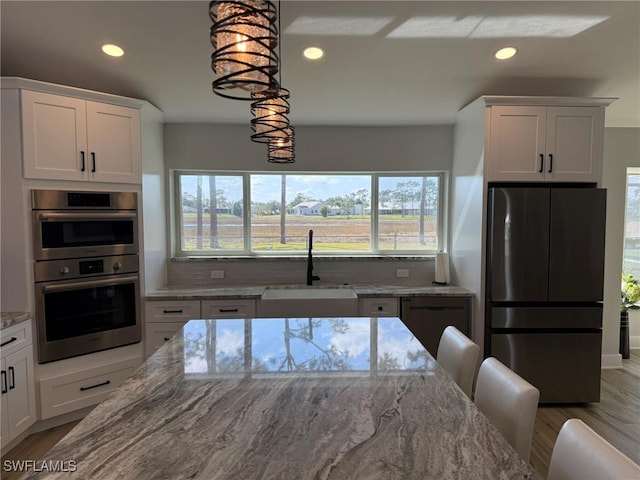 kitchen featuring light stone counters, appliances with stainless steel finishes, white cabinets, a sink, and wood finished floors