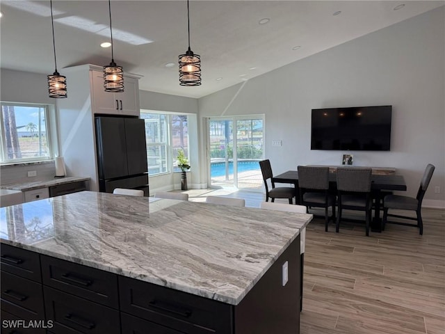 kitchen with light wood-type flooring, freestanding refrigerator, white cabinets, and light stone counters