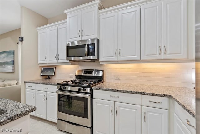 kitchen with appliances with stainless steel finishes, white cabinetry, light stone countertops, and tasteful backsplash