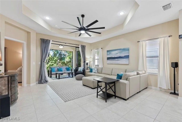 tiled living room with ceiling fan and a tray ceiling