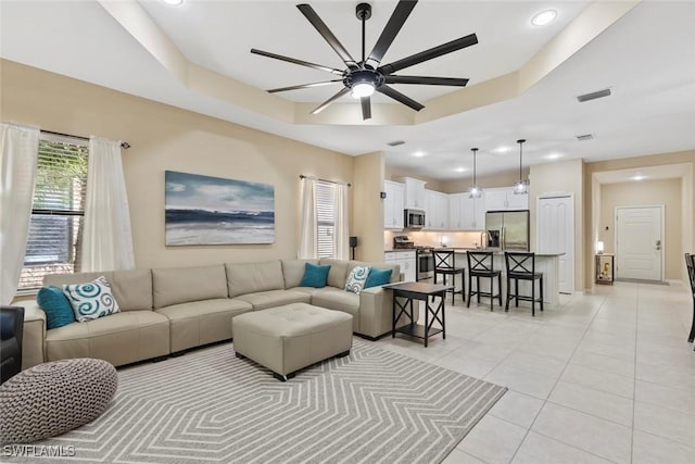 living room featuring a tray ceiling, light tile patterned flooring, and ceiling fan