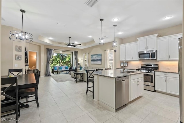 kitchen with white cabinetry, a kitchen island with sink, light stone countertops, appliances with stainless steel finishes, and pendant lighting