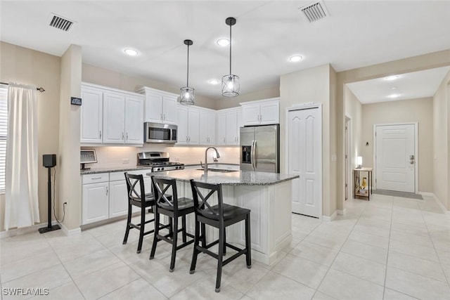 kitchen with appliances with stainless steel finishes, dark stone counters, white cabinets, sink, and a kitchen island with sink