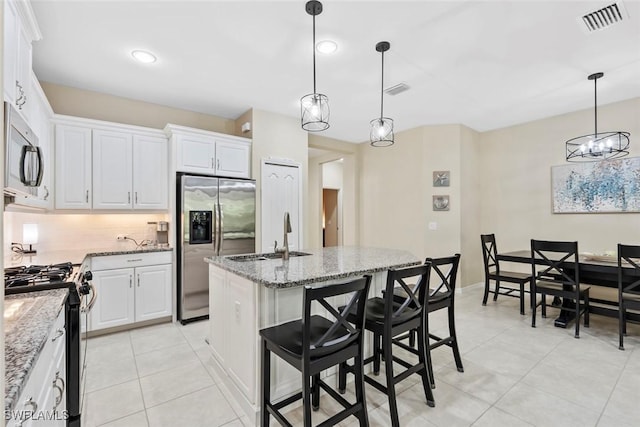 kitchen with appliances with stainless steel finishes, light stone counters, pendant lighting, white cabinets, and an island with sink