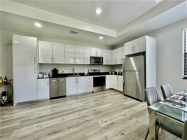 kitchen with sink, stainless steel appliances, a textured ceiling, white cabinets, and light wood-type flooring