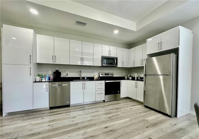 kitchen with appliances with stainless steel finishes, sink, white cabinets, and light wood-type flooring