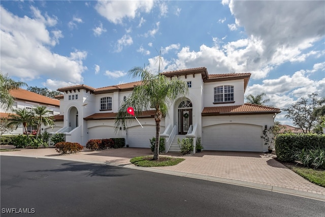 mediterranean / spanish-style house with a garage, decorative driveway, a tiled roof, and stucco siding