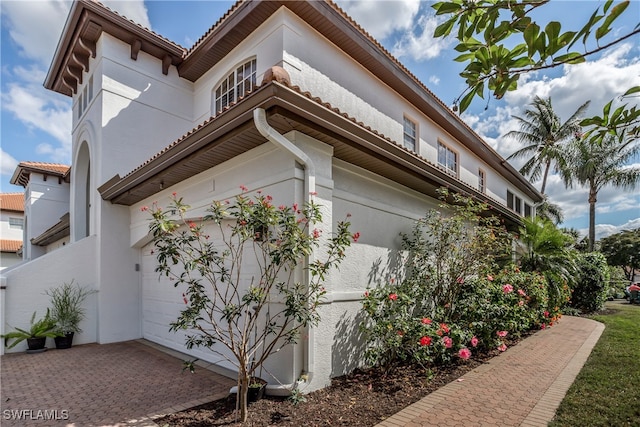 view of side of property with a tile roof, decorative driveway, and stucco siding