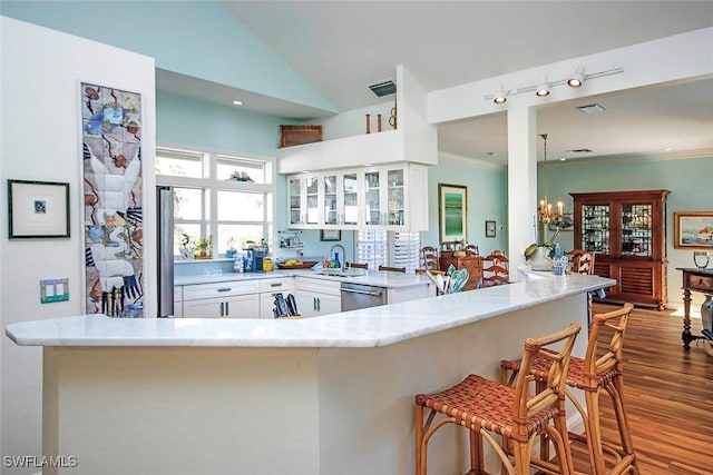 kitchen featuring crown molding, light hardwood / wood-style flooring, a breakfast bar area, white cabinets, and stainless steel dishwasher