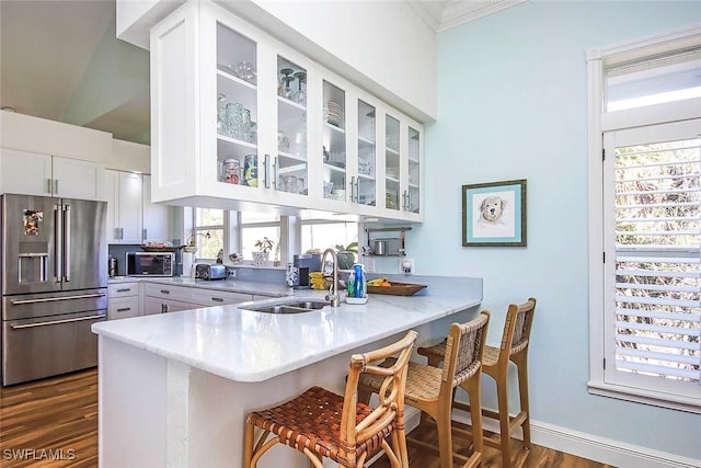 kitchen with high end refrigerator, kitchen peninsula, sink, and white cabinets