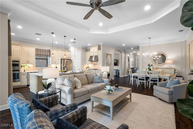 living room with a raised ceiling, wood-type flooring, ceiling fan with notable chandelier, and crown molding